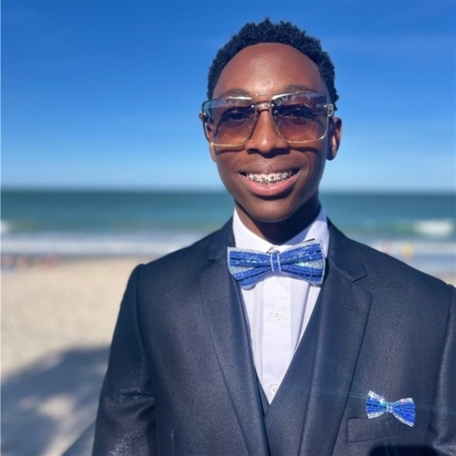 Portrait of Mustapha Strachan wearing a suit and blue bow tie at the beach